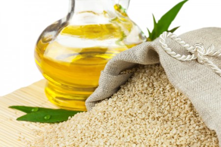 Macro view of sesame seeds in flax sack and glass bottle of sesame oil on mat isolated on white background